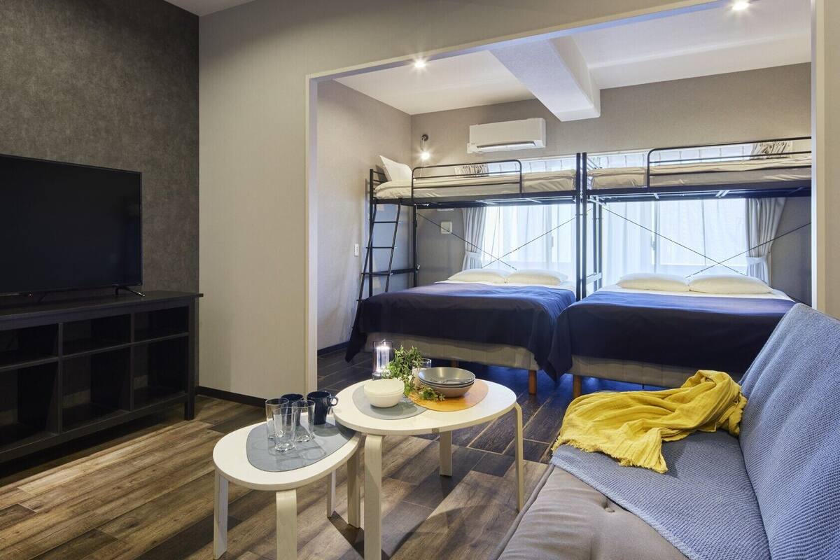 A compact room with bunk beds, a television, a small table, and a sofa.
