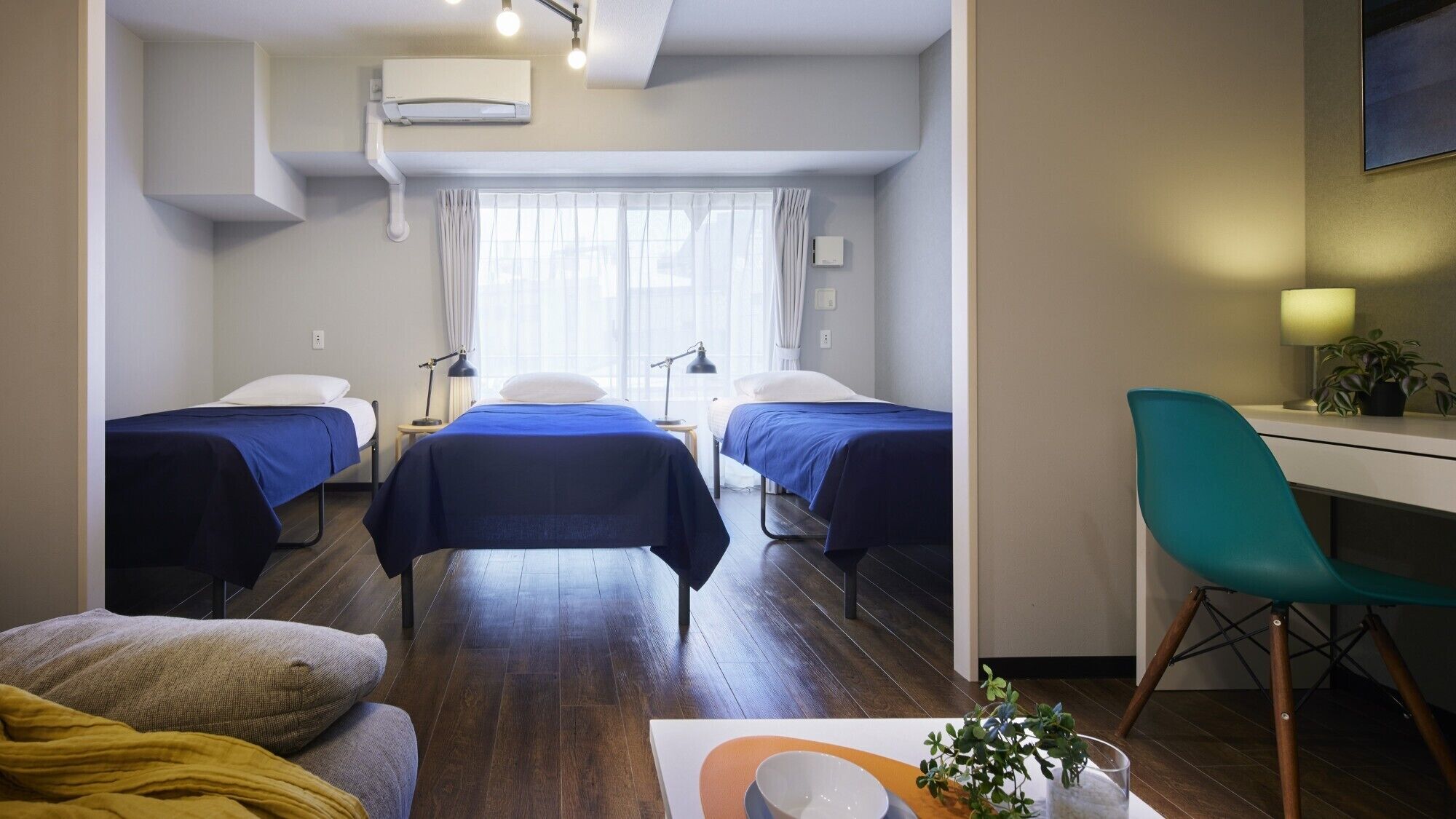 A hotel room with two single beds, a desk, a chair, a lamp, and a potted plant.