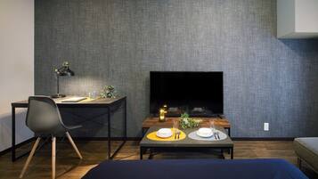 Habitació moderna amb escriptori, cadira, televisió i zona de dinar amb taula per a dues persones.