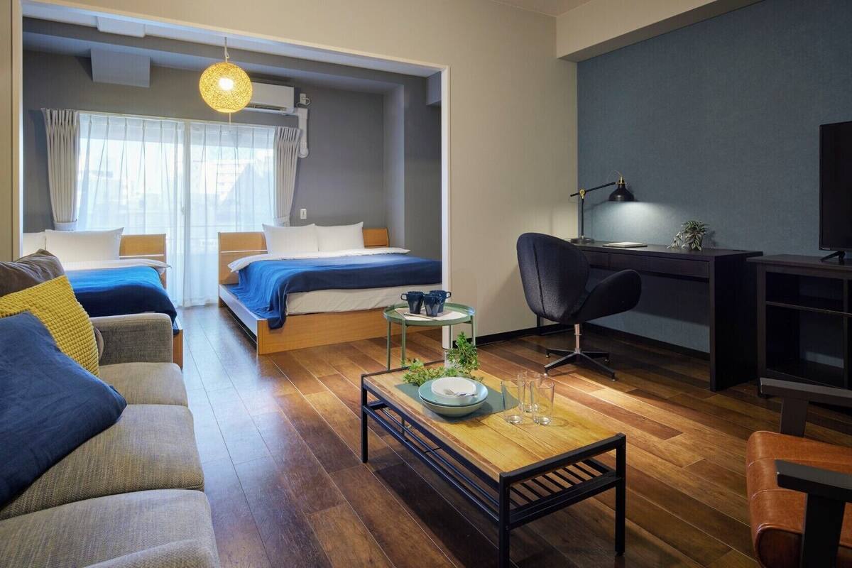 A modern hotel room with a sofa, two beds, a desk, and a TV.