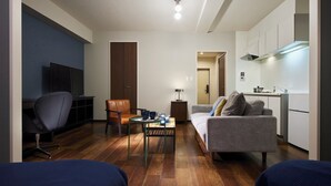 A modern living room with a sofa, a coffee table, a TV, and a dining area. - Minn Juso (Osaka)