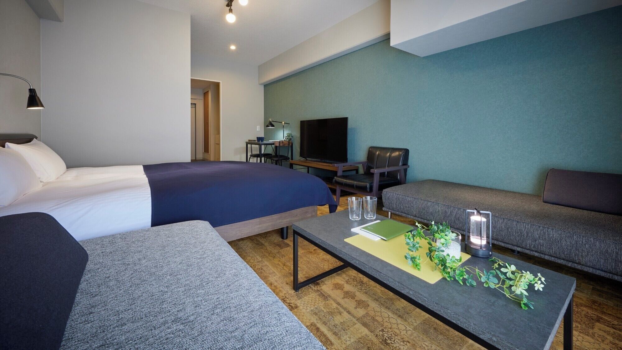 Una habitación de hotel moderna con una cama grande, un sofá, una mesita con una planta y un televisor.