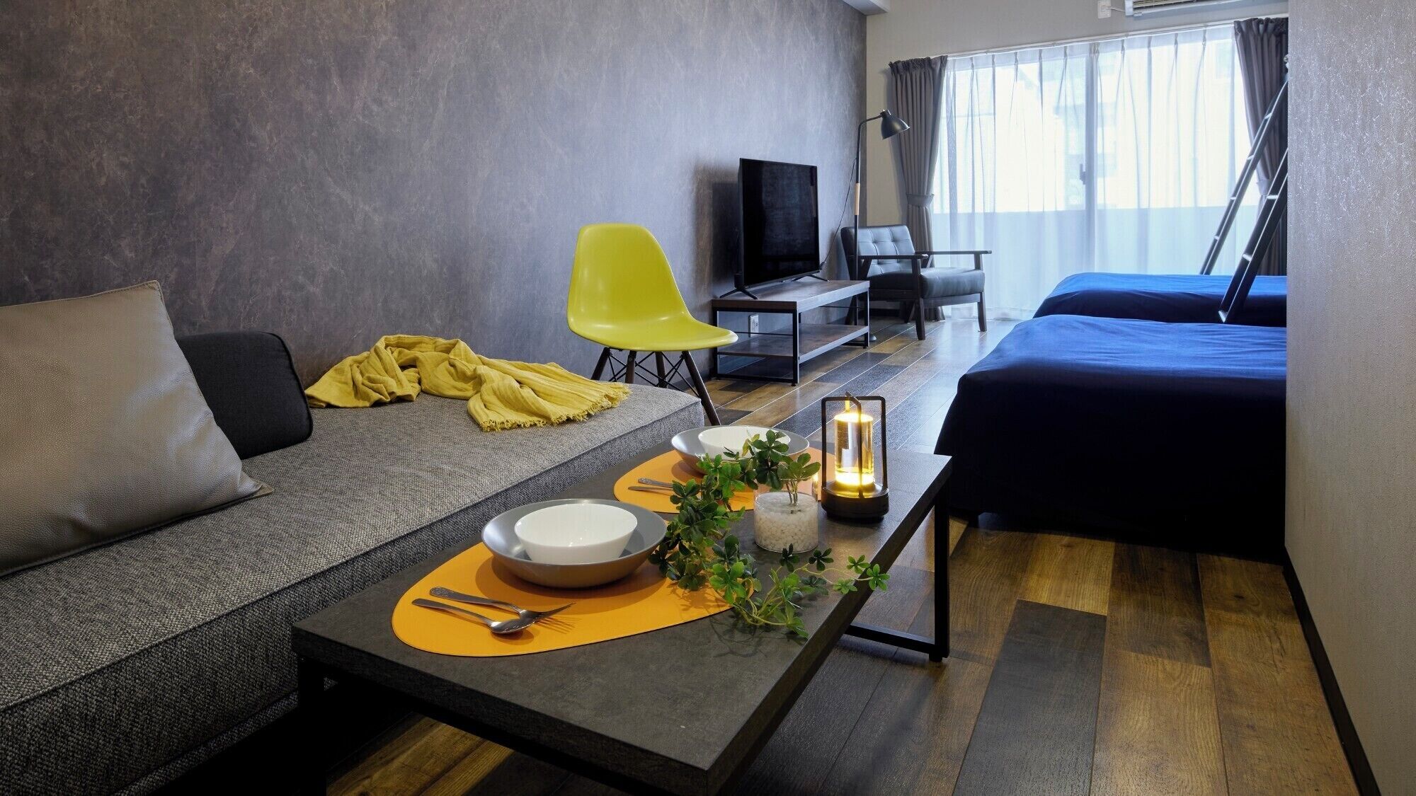 A modern hotel room with a sofa, a bed, a dining table with a candle, and a TV.