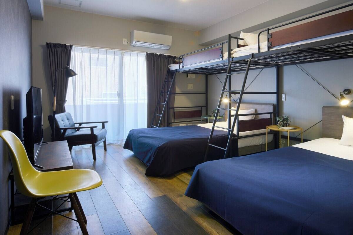 A hotel room with bunk beds, a desk with a chair, a television, and a small table with a plant.
