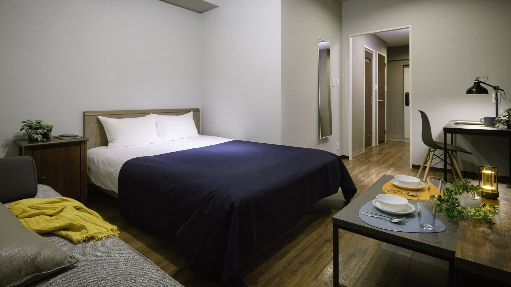 A hotel room with a bed, bedside table, chair, and a small dining table with plates and a candle.