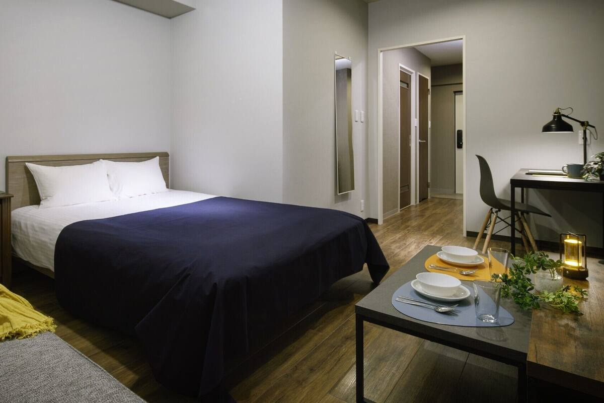 A hotel room with a bed, bedside table, chair, and a small dining table with plates and a candle.