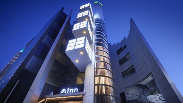 A modern building with a prominent 'Inn' sign, featuring a unique architectural design with a curved facade and a central cylindrical structure. - Minn Juso (Osaka)