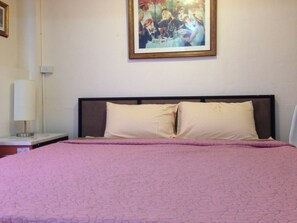 Un dormitorio con cama, mesita de noche, lámpara y un cuadro en la pared.