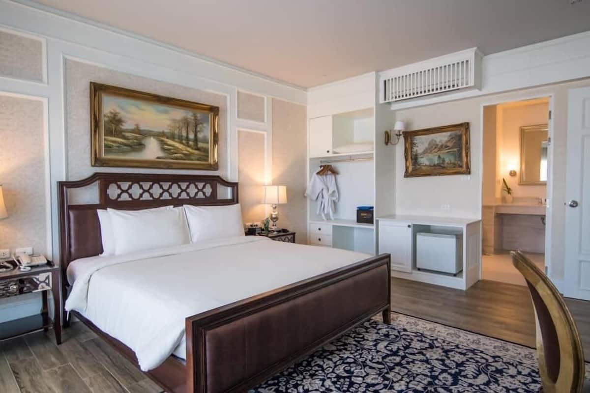 A hotel room with a large bed, a bedside table with a lamp, a dresser, a mirror, and a painting on the wall.