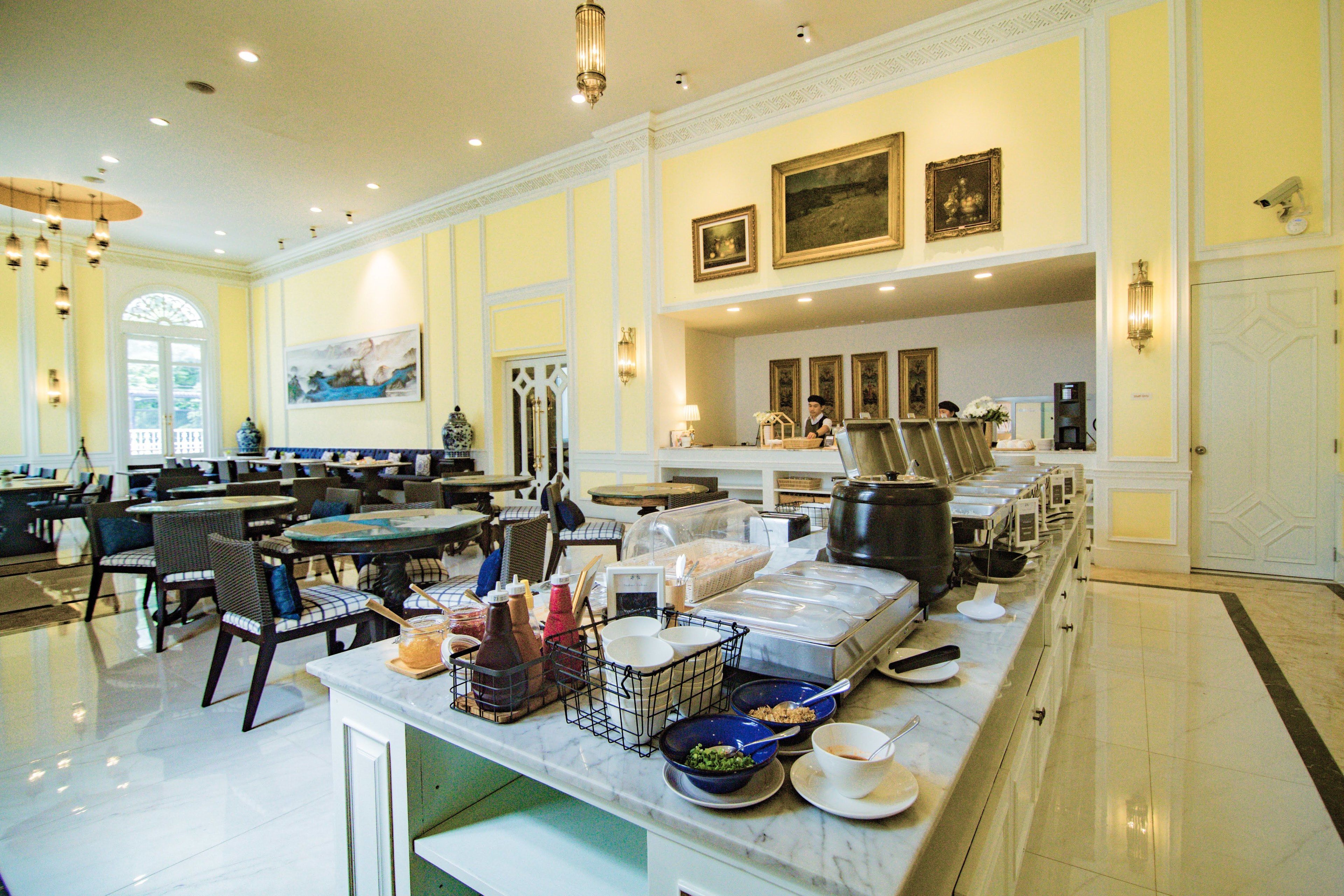 Un grand espace dédié à la salle à manger, avec de nombreuses tables et chaises, un buffet proposant une variété de plats, et un mur décoratif orné d’œuvres d’art encadrées.