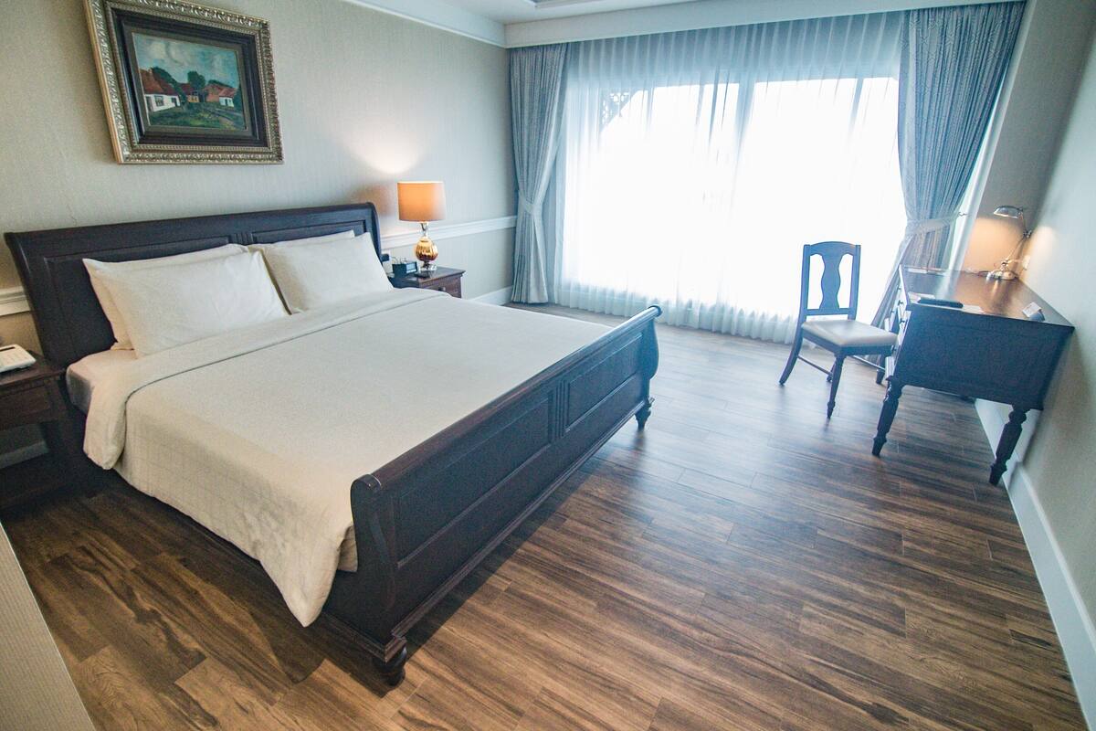 A hotel room with a large bed, a desk, a chair, and a window with curtains.