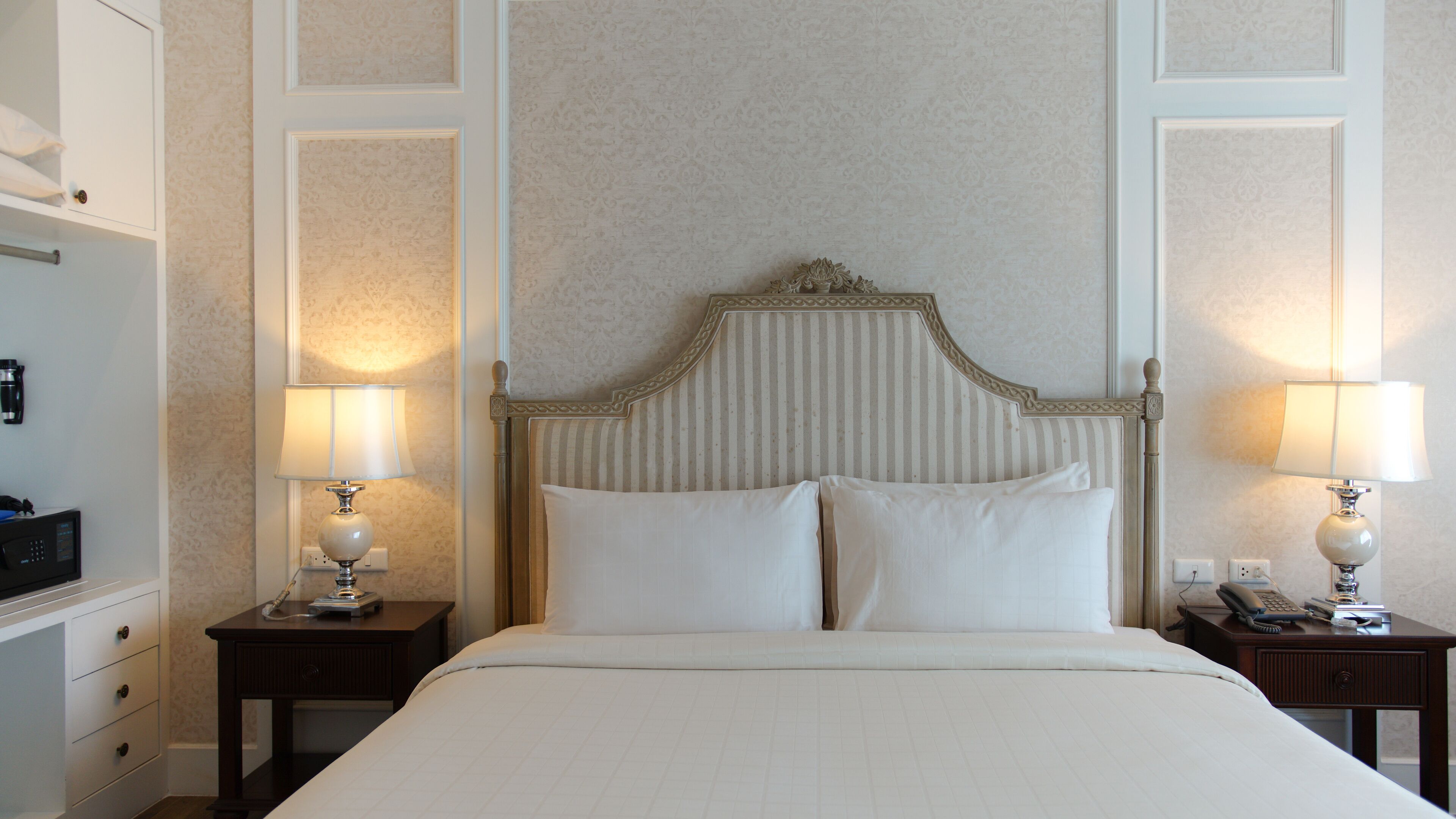 A neatly made bed with a wooden headboard, two bedside tables with lamps, and a wall with a decorative panel.