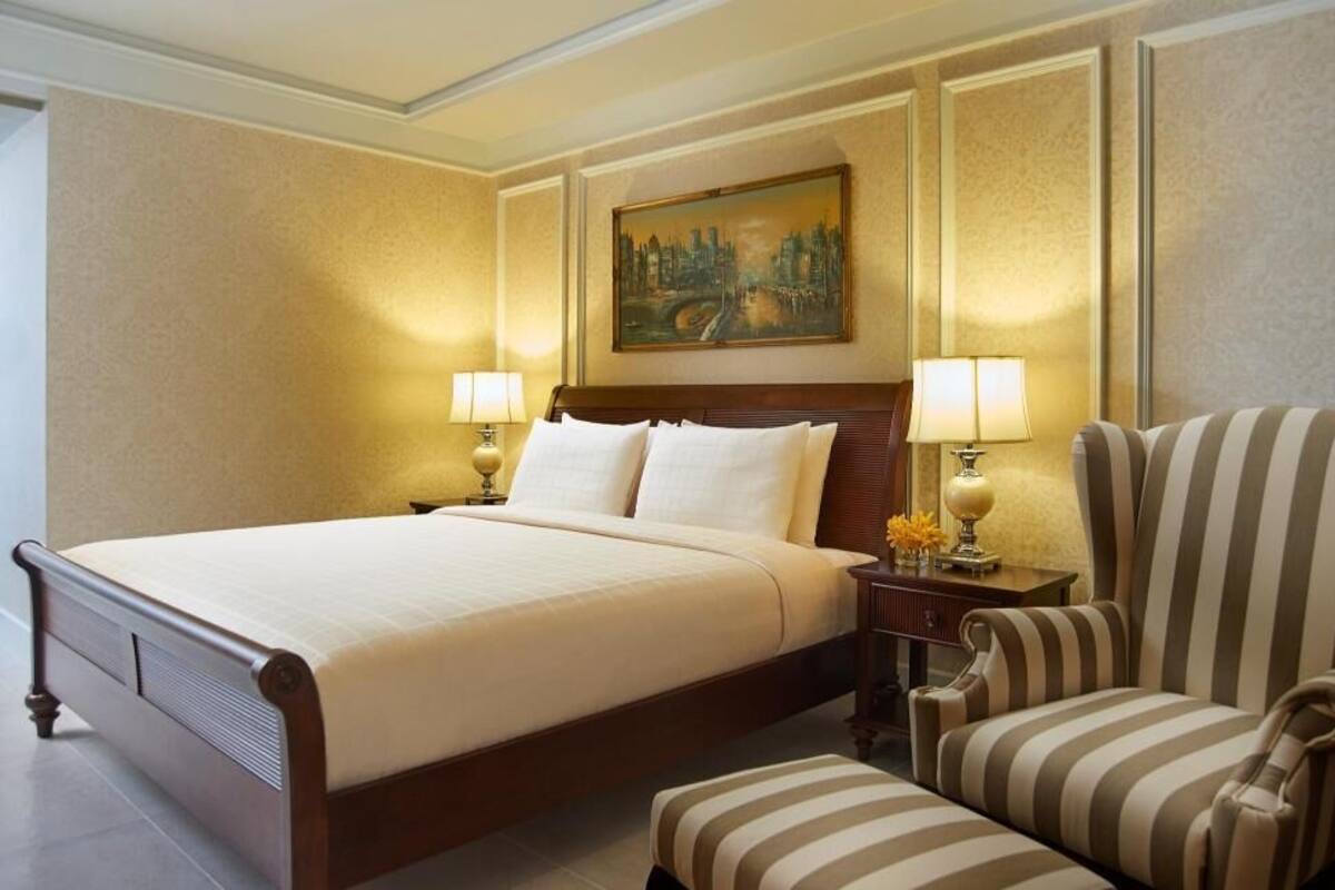 A hotel room with a large bed, two bedside lamps, a striped armchair, and a painting on the wall.