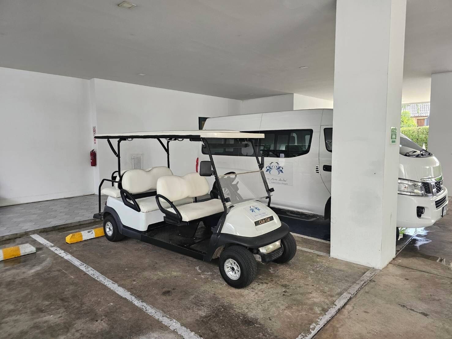Un parcheggio con un golf cart, un furgone bianco e un camioncino bianco.