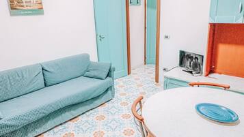 Una habitación con un sofá azul estampado, una mesa redonda con sillas y un suelo de baldosas con motivos florales.