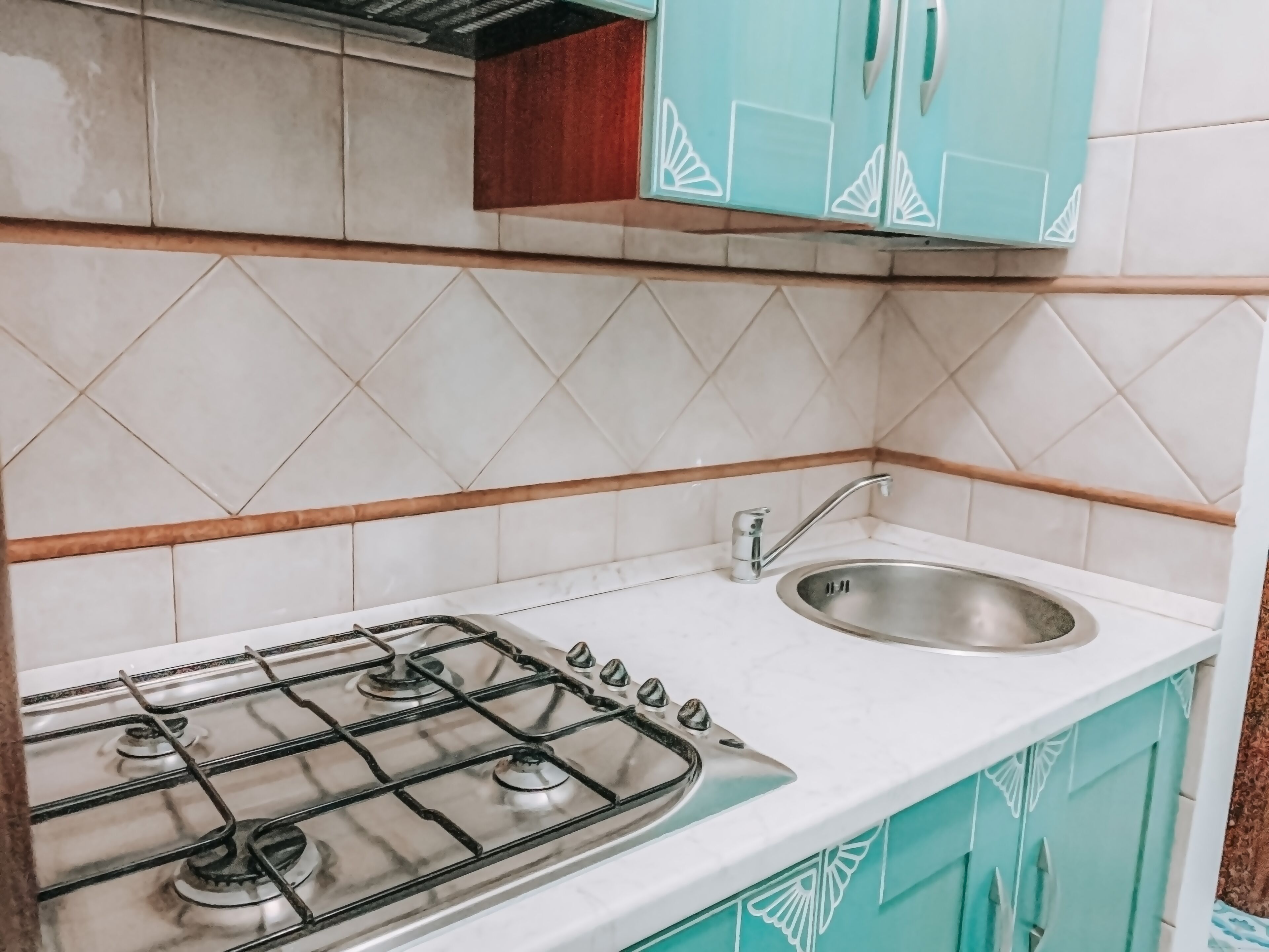 A kitchen with a gas stove, a sink, and teal cabinets.