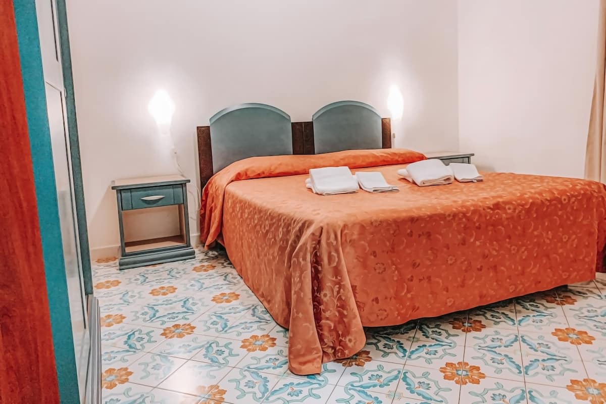 Una habitación de hotel con una cama, una mesita de noche y suelo de baldosas.