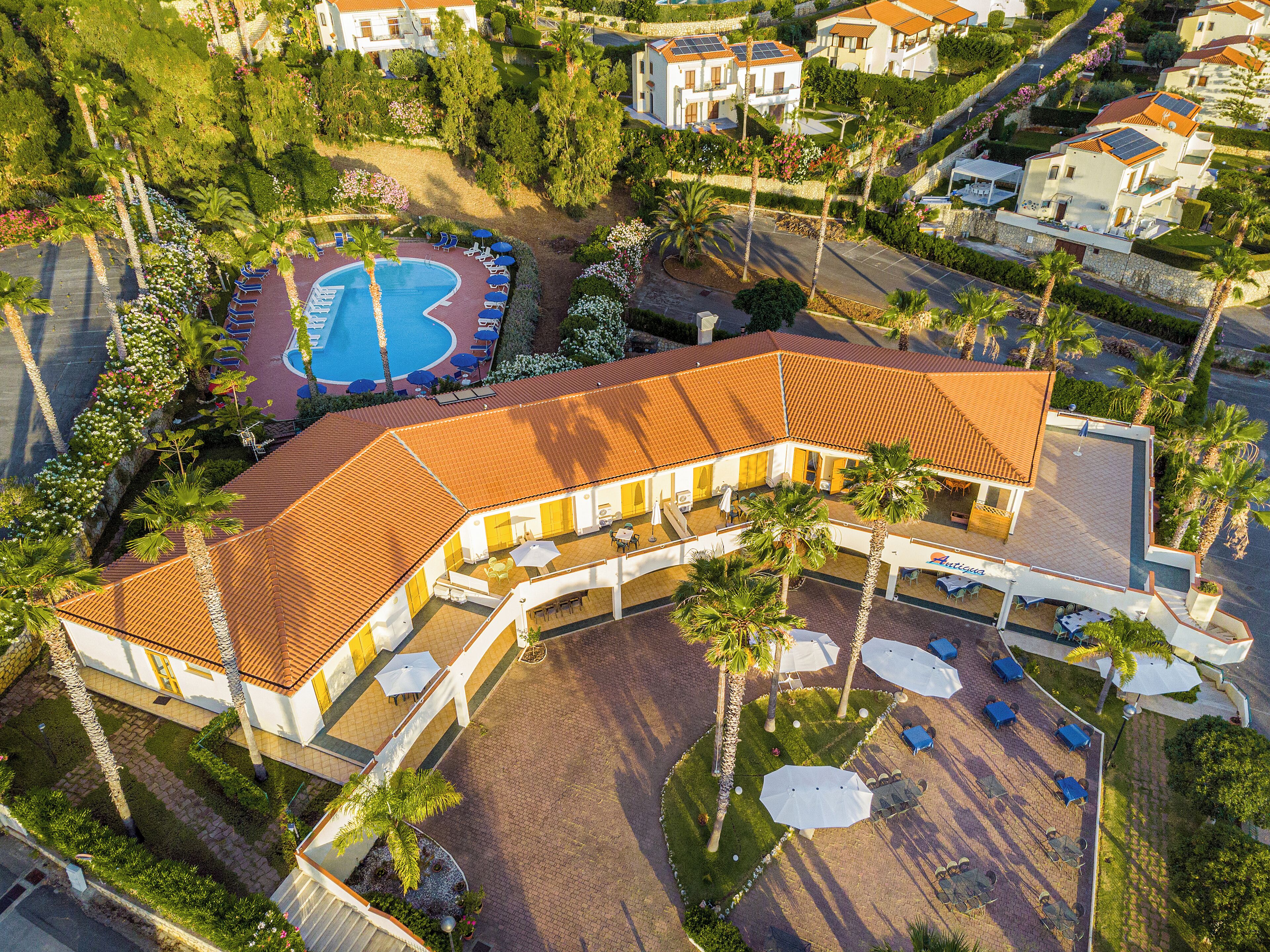 An aerial view of a resort with a swimming pool, outdoor seating, and palm trees.