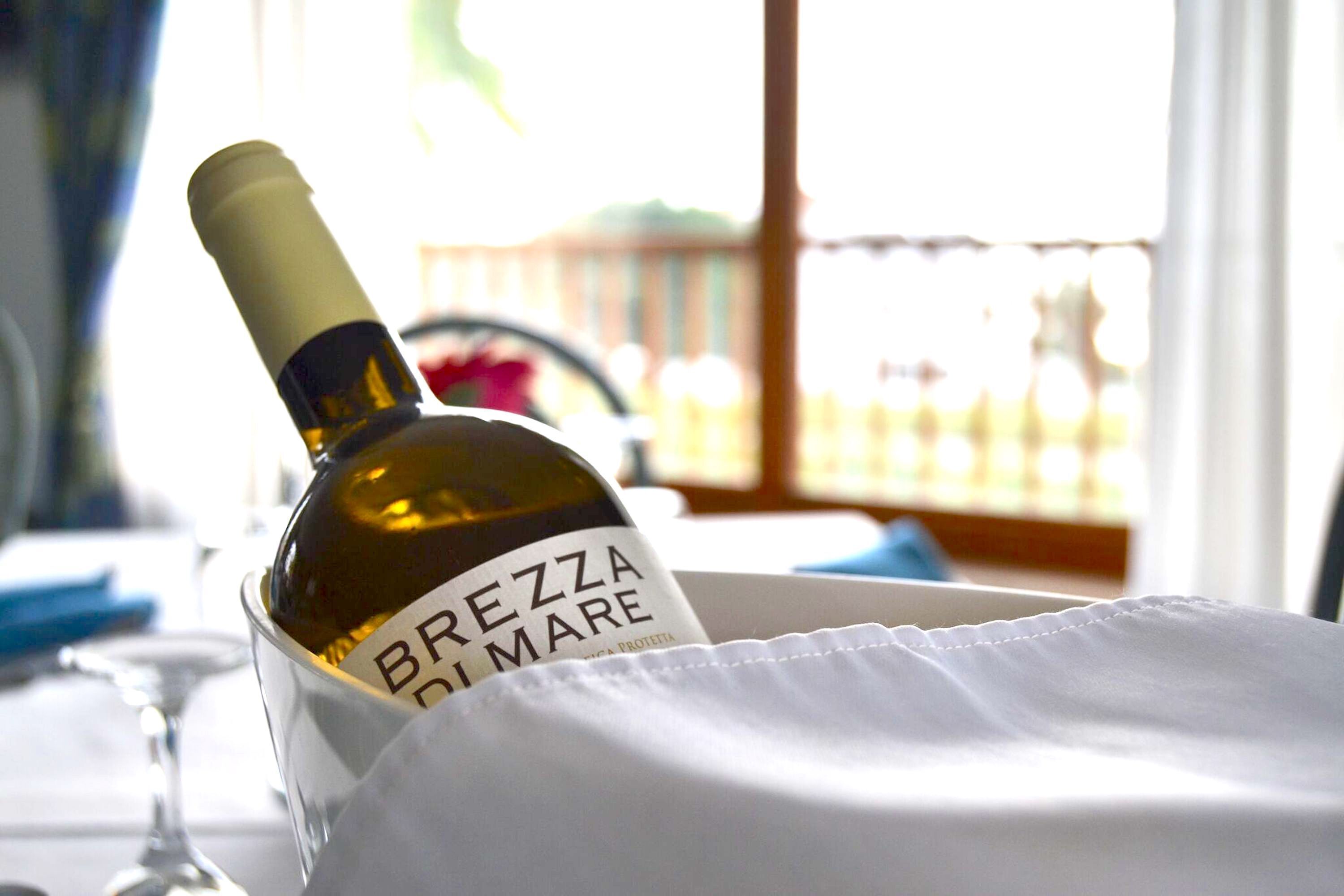Eine Flasche BREZZA DI MARE Wein in einem Glasbehälter auf einem Tisch mit einer weißen Serviete.