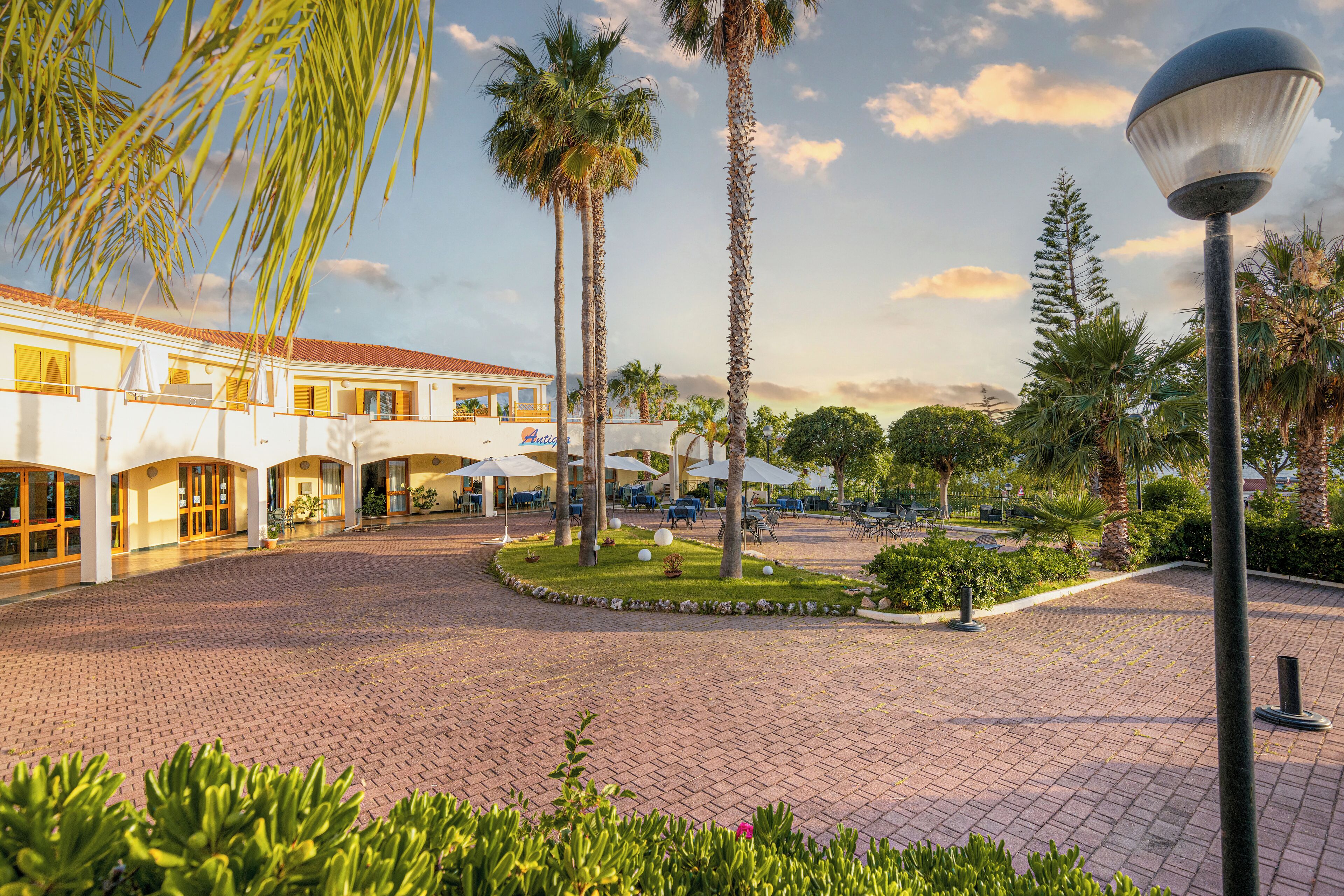 A courtyard with palm trees, a building with a tiled roof, and outdoor seating.
