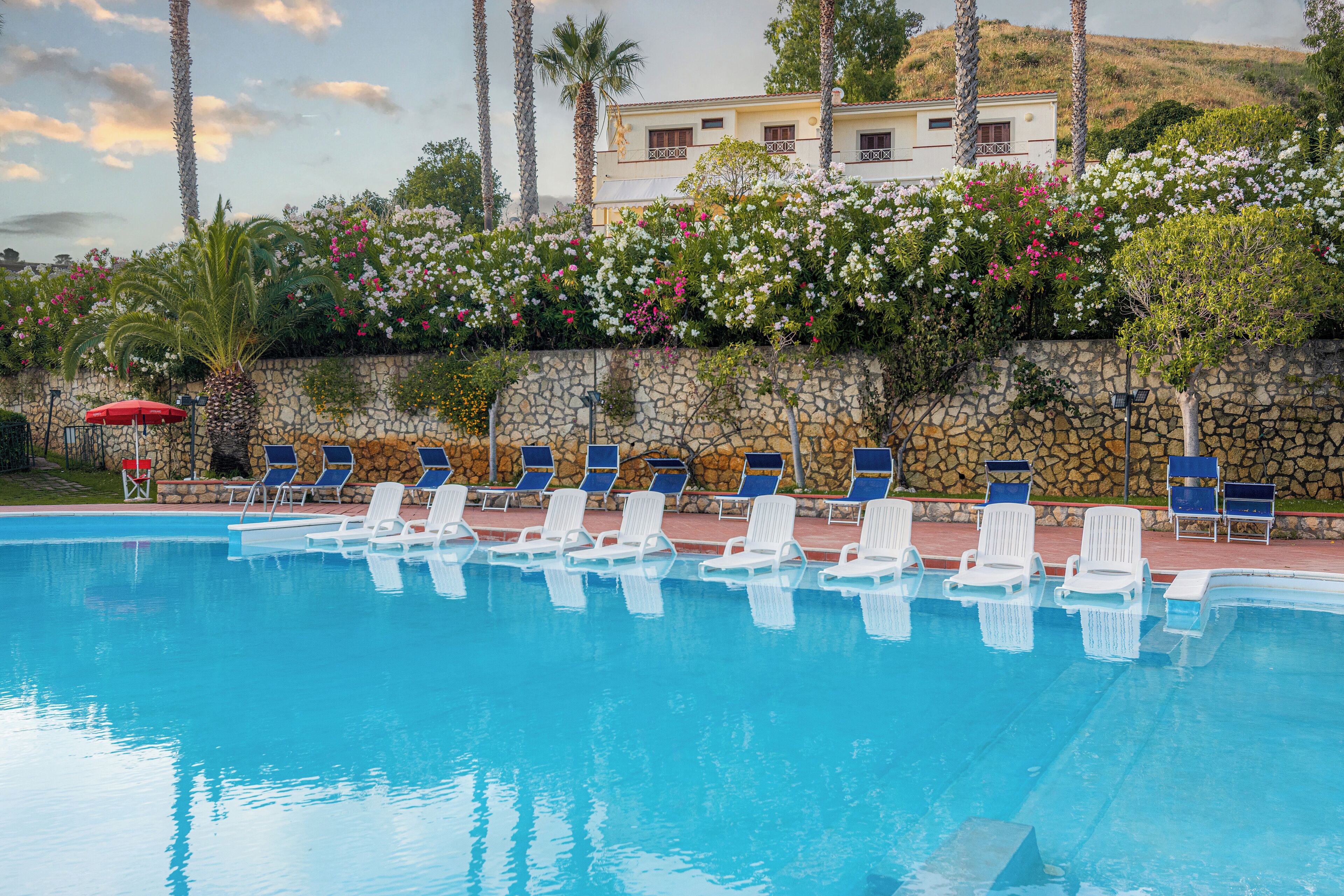 Une piscine avec des chaises longues, un mur en pierre et un bâtiment en arrière-plan.