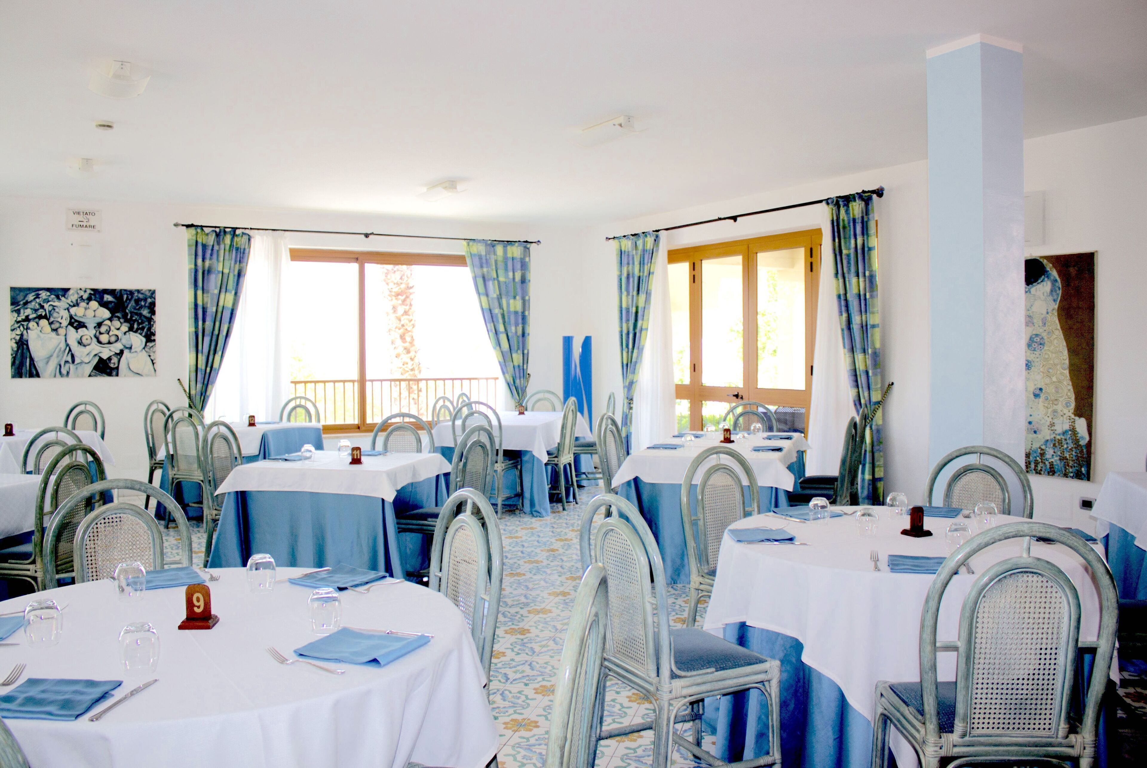 Un comedor con mesas redondas, sillas y manteles azules.