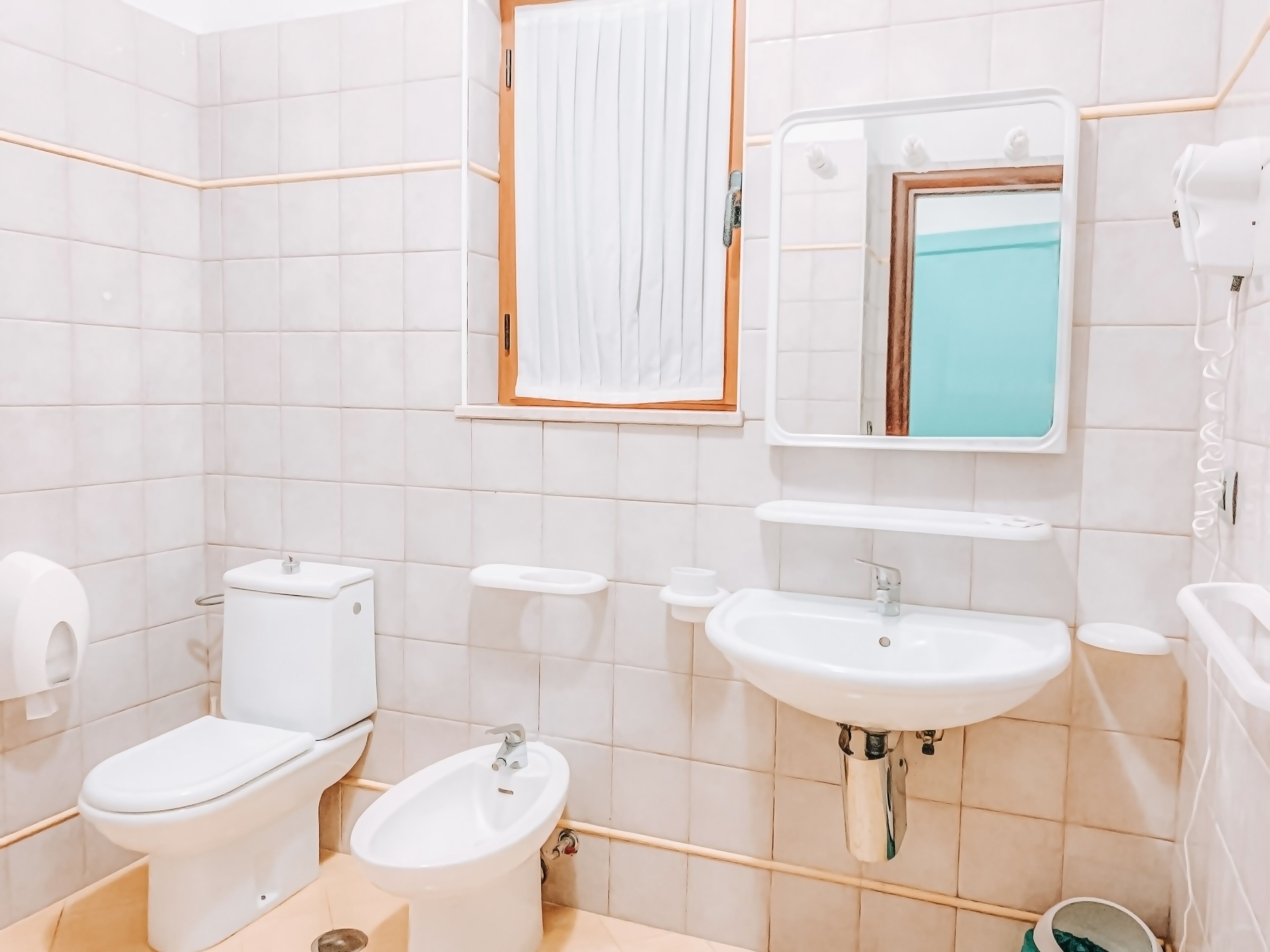 Un baño con inodoro, bidé, lavamanos y espejo.