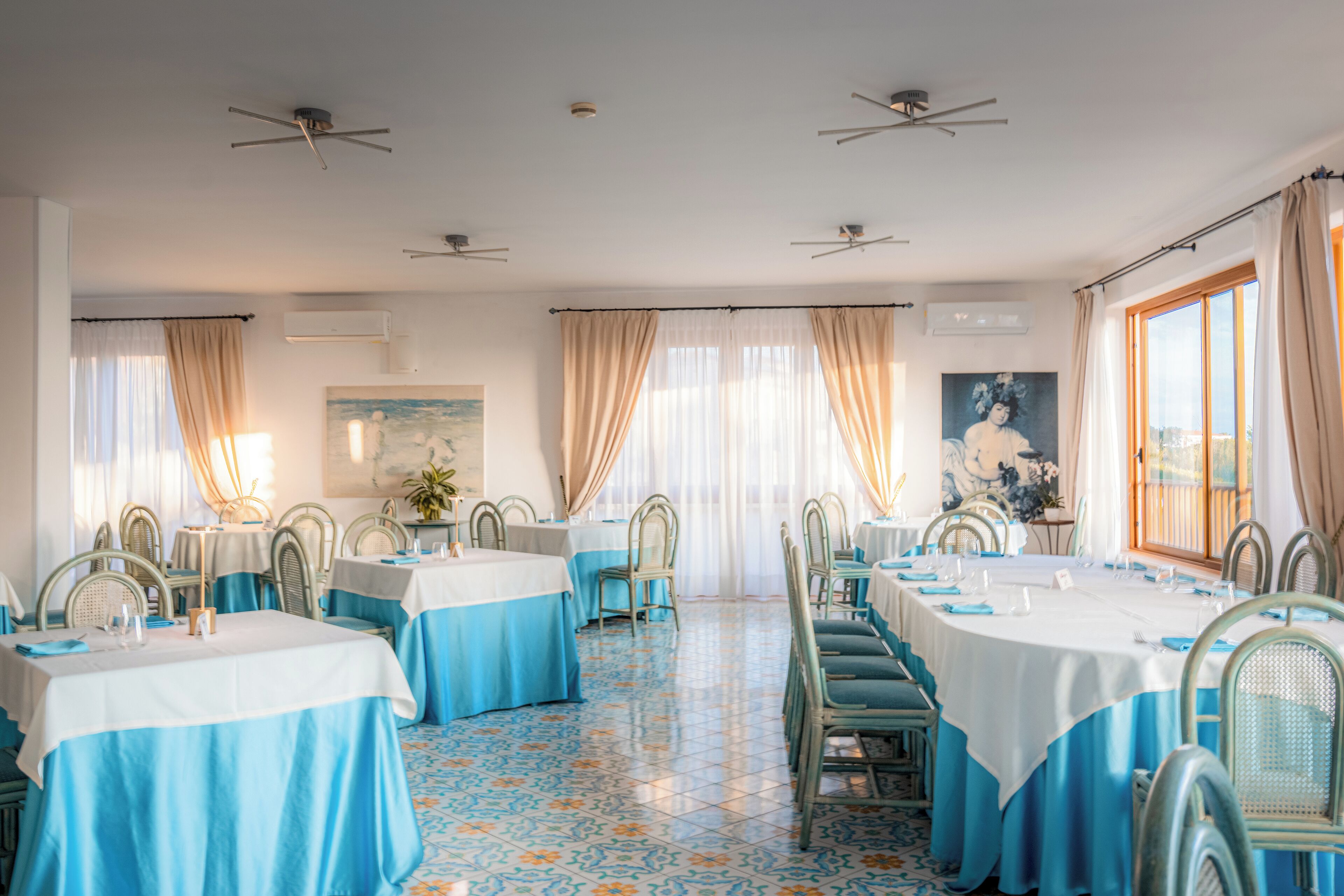 A dining area with tables set for service, chairs, ceiling fans, and a large window with curtains.
