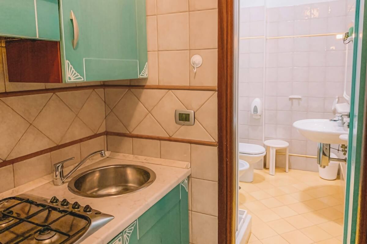 Una cocina con estufa a gas, lavamanos y gabinetes color turquesa.