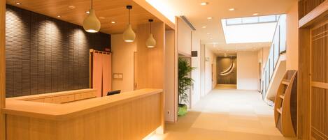 Un área de recepción moderna con un mostrador de madera, iluminación colgante y una escalera que conduce a un nivel superior.