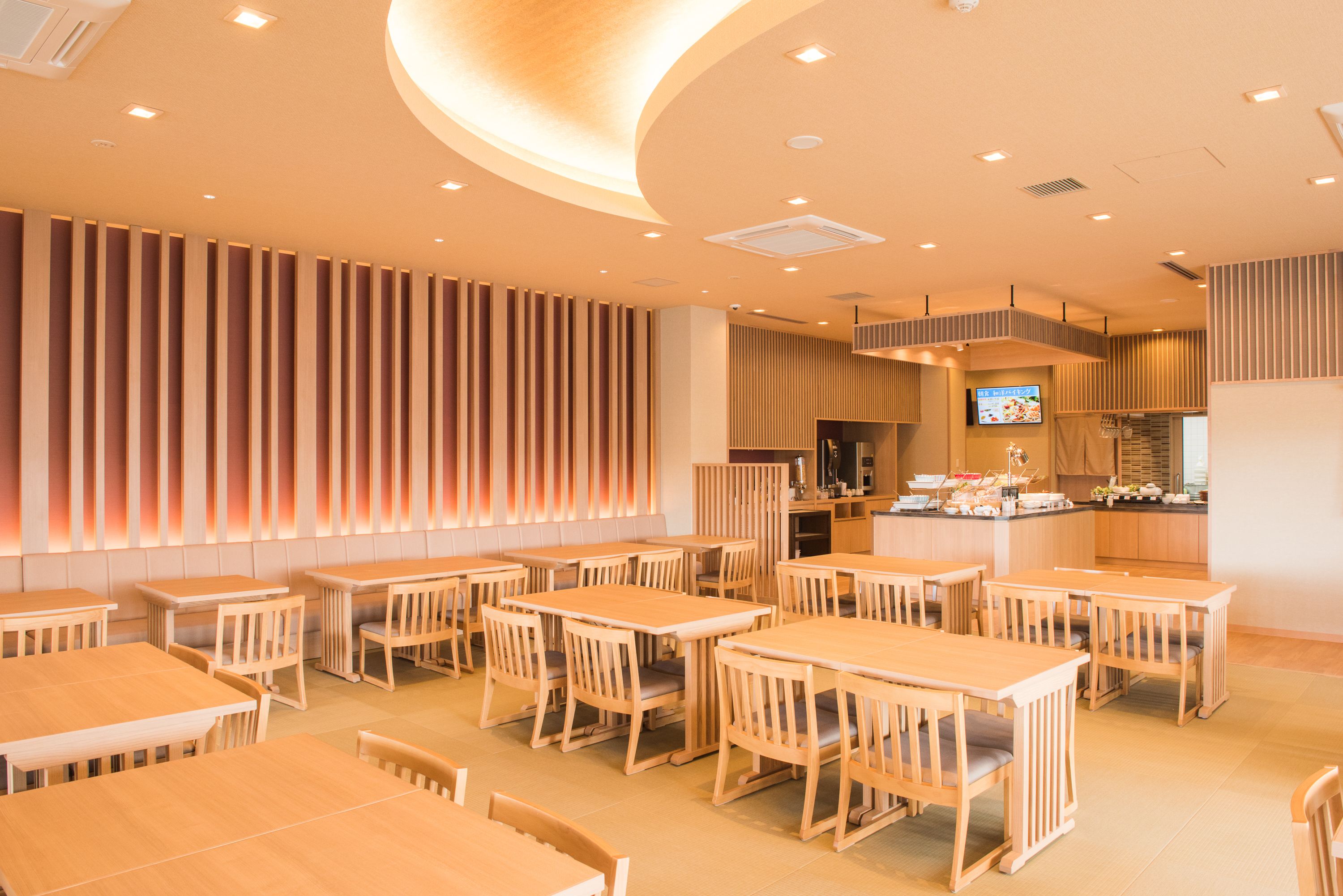 A restaurant with wooden tables and chairs, a kitchen area, and a TV screen.