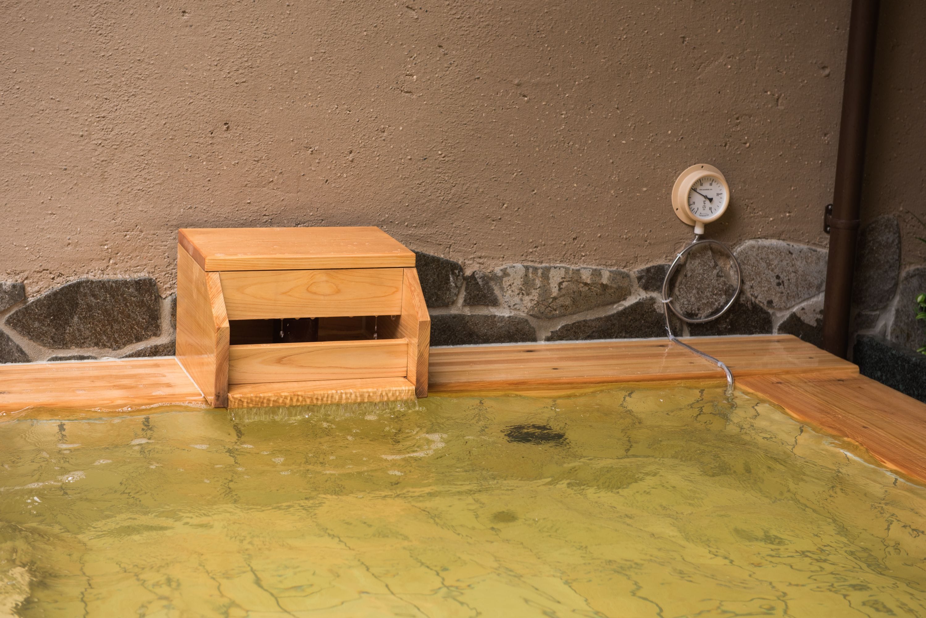 Un banco de madera junto a un manantial termal con un termómetro.