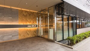 A modern building entrance with glass doors, a wooden herringbone wall, and a tiled floor.
