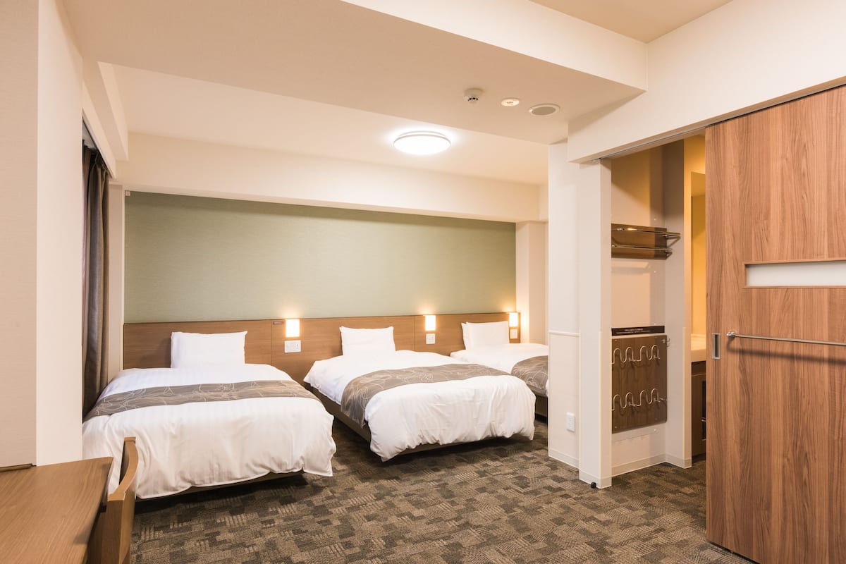 A hotel room with two beds, a wooden wardrobe, and a shower area.