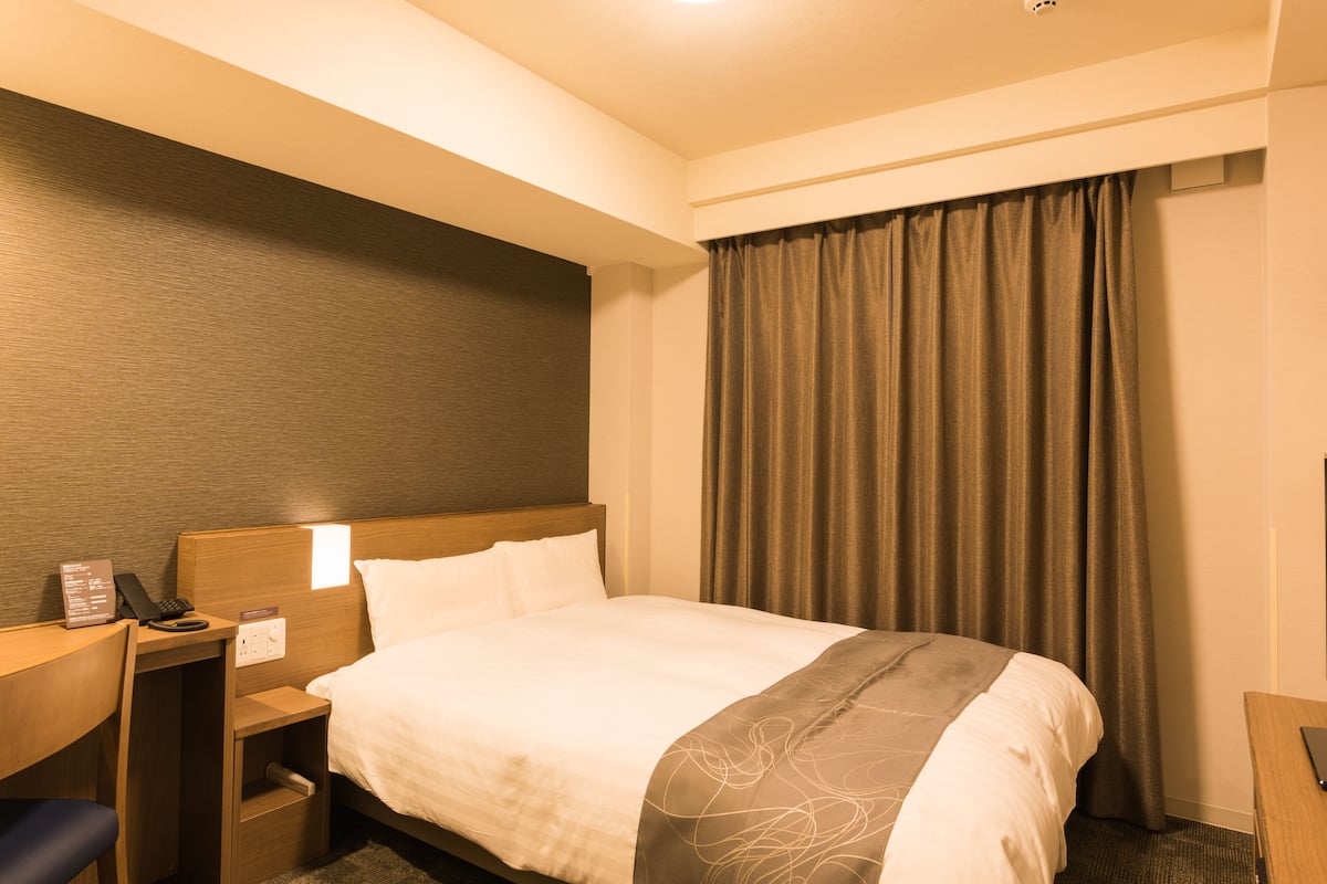 A hotel room with a bed, a desk with a telephone, and a window with curtains.