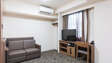 A compact living space with a sofa, a TV on a wooden stand, and a desk with a chair.