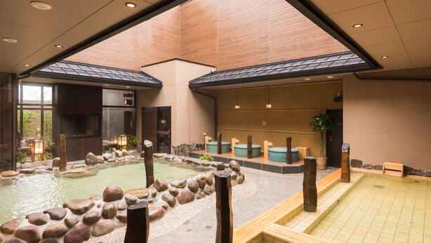 A traditional Japanese onsen with two hot spring pools, wooden benches, and a stone pathway.
