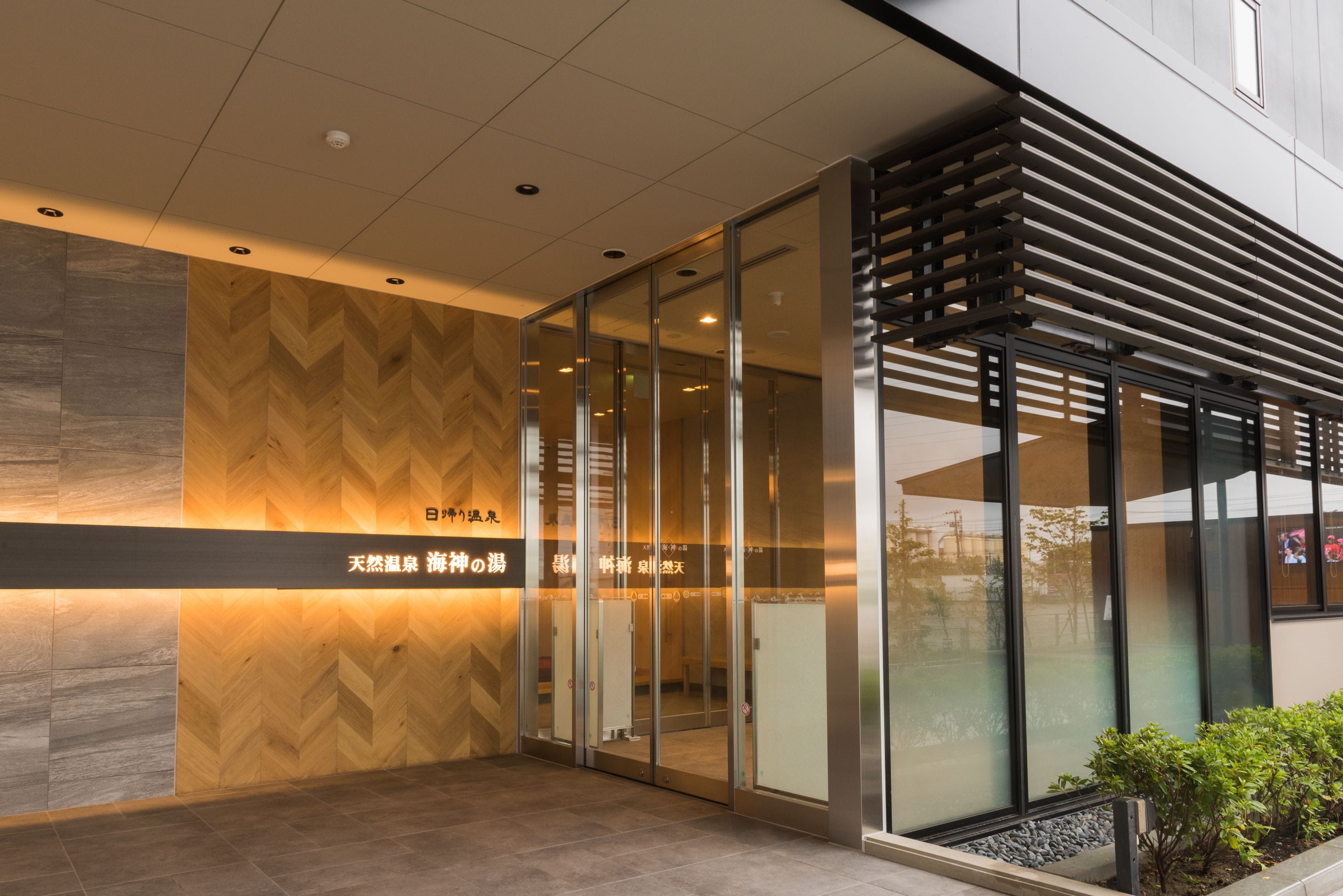 Una entrada moderna con puertas de vidrio, un muro de madera con diseño en chevron y un letrero con caracteres japoneses.