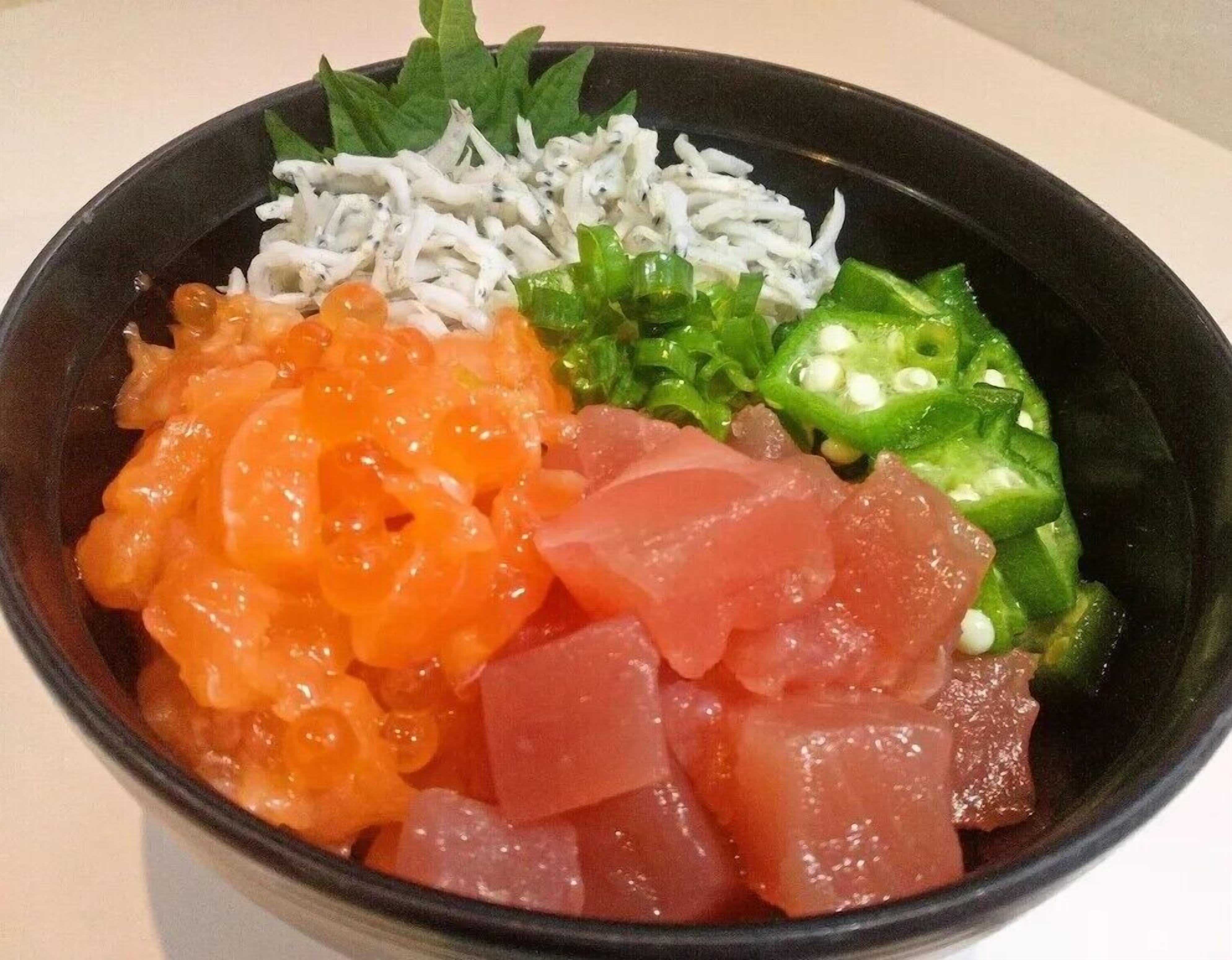 Uma tigela de sashimi com diversos acompanhamentos, incluindo peixe, legumes e possivelmente algum arroz.