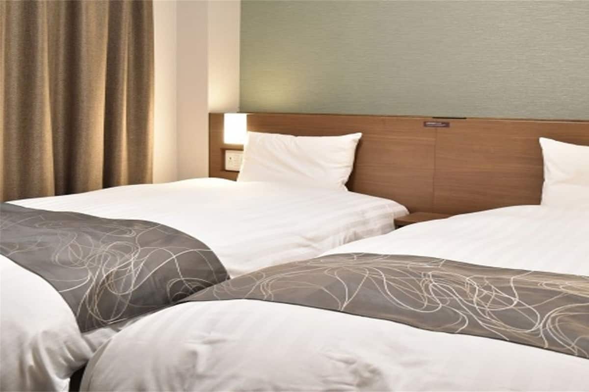 A hotel room with two beds, each with a wooden headboard, white bedding, and a patterned throw blanket.