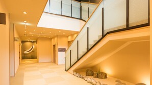 A modern hotel corridor with a checkered floor, a glass railing on the staircase, and a sign indicating a hotel room.