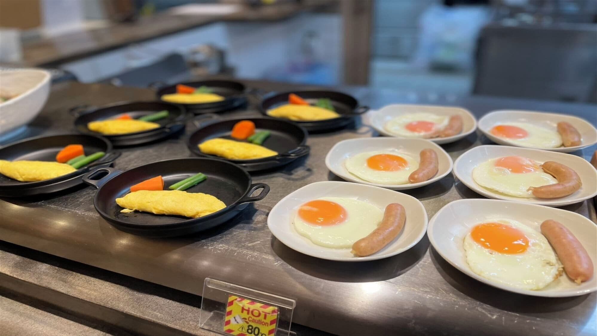 Un buffet proposant divers plats pour le petit-déjeuner, notamment des omelettes, des saucisses et des légumes.