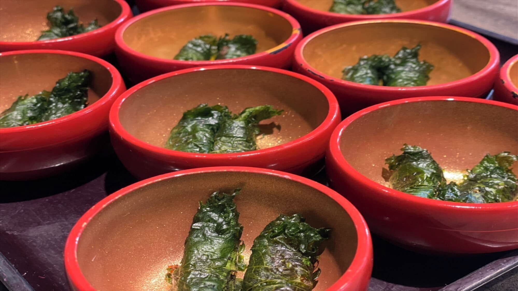A tray of red bowls containing cooked greens.
