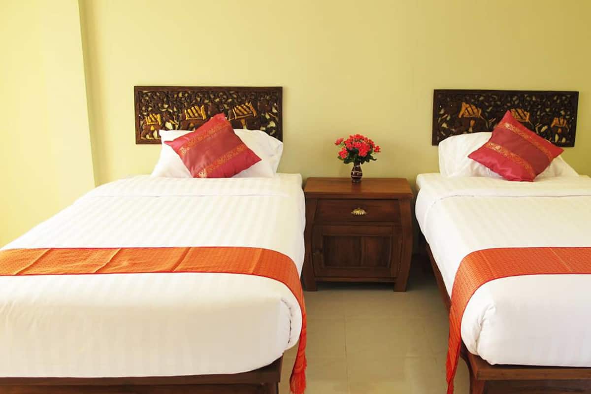A hotel room with two beds, each with white bedding and orange accents, a nightstand with a vase of flowers, and artwork on the walls.
