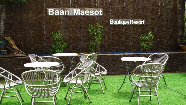 Outdoor seating with metal chairs and tables, a brick wall, and a sign reading "Baan Maesot Boutique Resort". - Baan Maesot Boutique Resort (Mae Sot)
