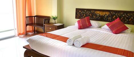 A hotel room with a large bed, a wooden nightstand, a chair, and a window with curtains.
