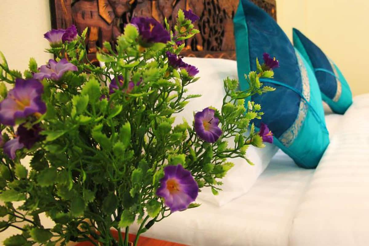 A bed with white bedding and a potted plant with purple flowers.