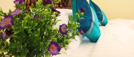 A bed with white bedding and a potted plant with purple flowers.