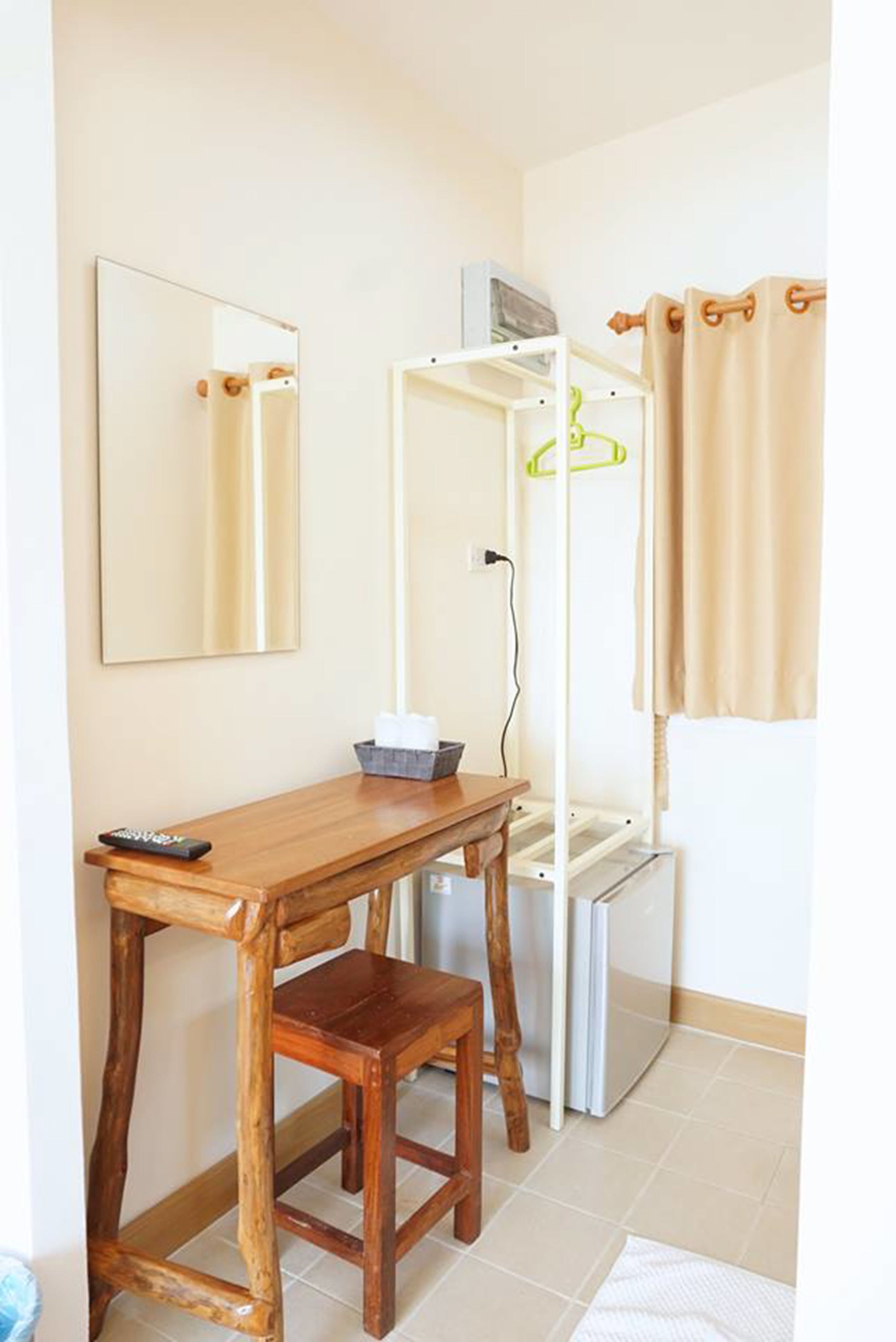 A small room with a wooden table and chair, a mirror, a white cabinet, and a shower area.