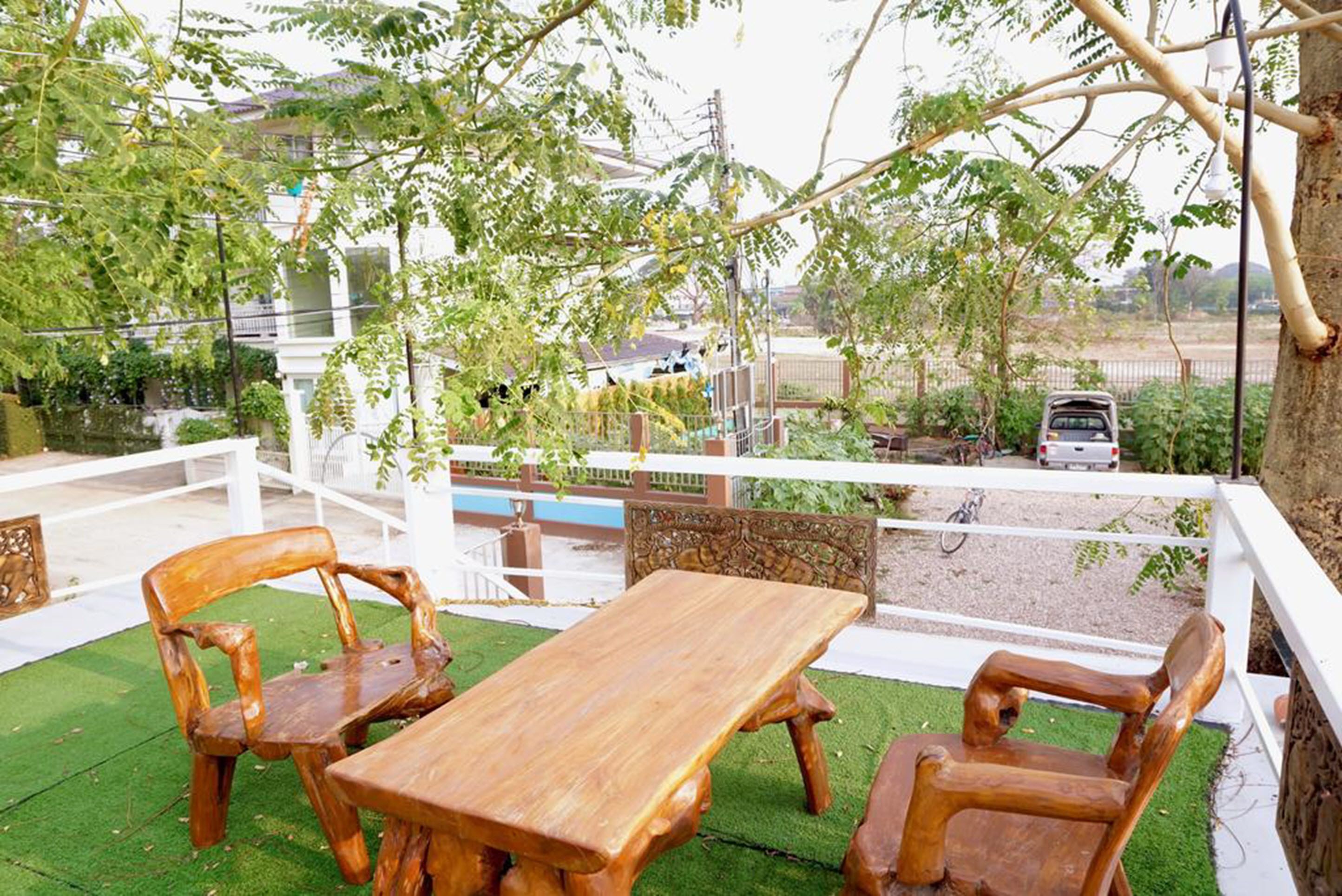 An outdoor seating area with a wooden table and chairs, surrounded by greenery and a view of a residential area.